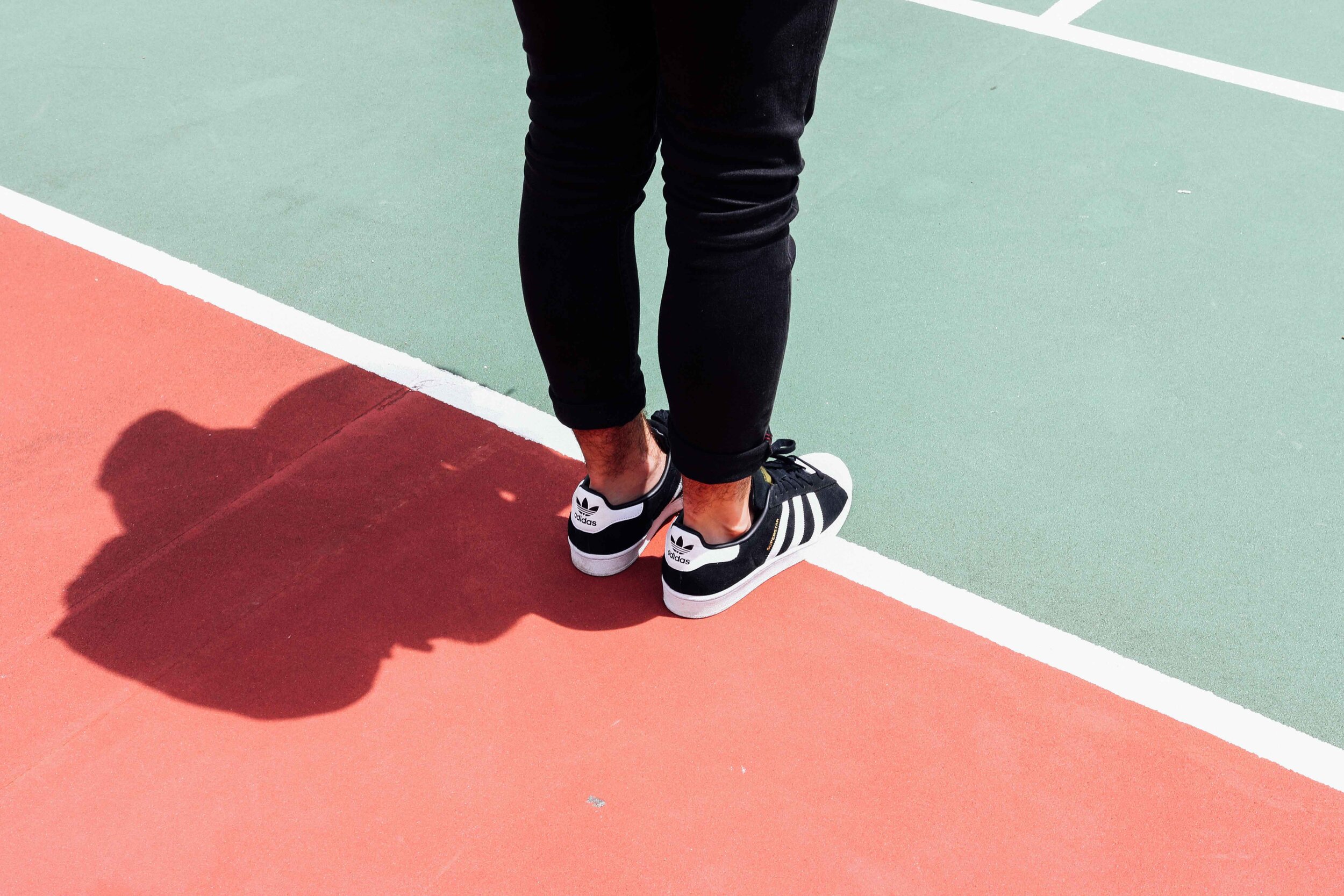 Person in black sneakers standing straight on white track line with no forward momentum. On either side of the white line is a red and light green track surface. There's a stark dark shadow behind them meant to represent time passing on the "5K walk/run" fundraisers many nonprofits host.